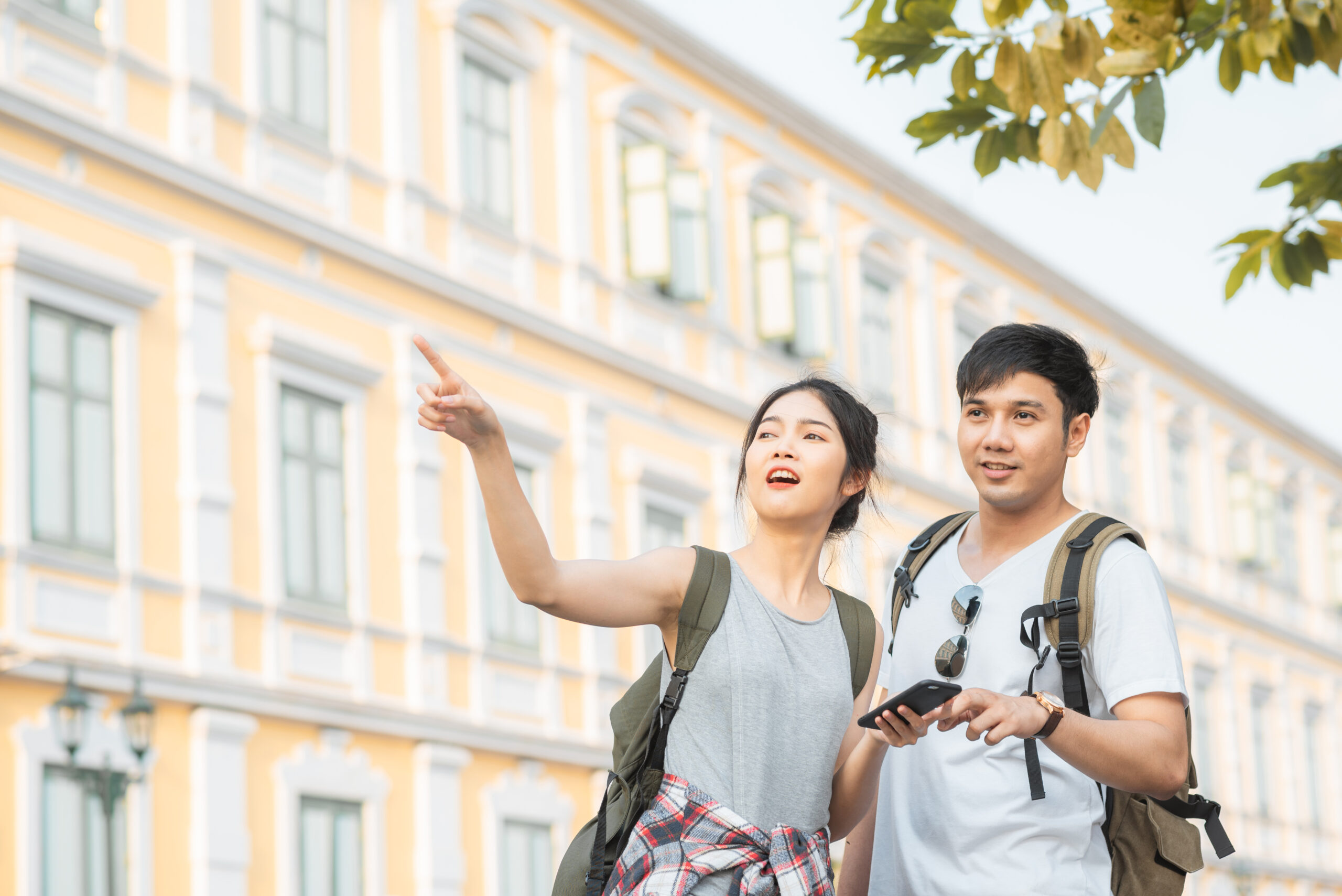 Traveler Asian couple direction on location map in Bangkok, Thailand, couple using mobile phone looking on map find landmark while spending holiday trip. Lifestyle couple travel in city concept.